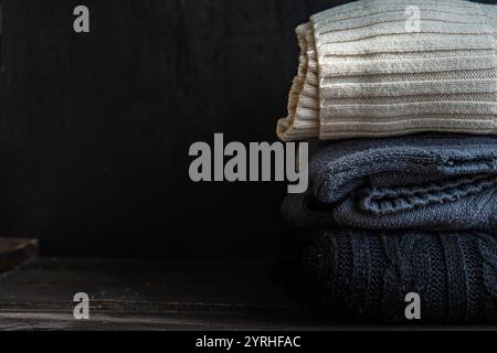 A neatly folded stack of cozy knitted sweaters in neutral tones lies on a rustic wooden surface, showcasing a warm and stylish fashion statement for c Stock Photo