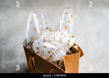 A close-up of a stylish brown gift bag with white tissue paper adorned with golden stars The image captures the essence of celebration, surprise, and Stock Photo