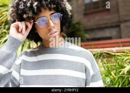 A mixed race woman with vitiligo enjoys a calm and relaxing day at the university campus, wearing stylish round sunglasses and a striped sweater, surr Stock Photo