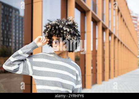 A mixed race woman with vitiligo wearing sunglasses and a striped sweater, enjoying a relaxing day at a modern university campus Reflections on the gl Stock Photo