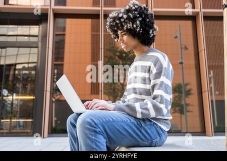 A mixed race woman with vitiligo sits outdoors at a university campus, using a laptop She is focused and content, epitomizing a calm, scholarly atmosp Stock Photo
