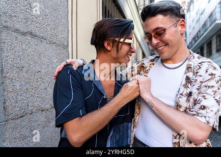 Two stylish young gay men share a joyful, playful moment together while casually dressed and walking in an urban setting, demonstrating a close, affec Stock Photo
