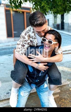 A joyful young couple shares a playful and affectionate moment on a sunny day, as one carries the other piggyback, both laughing and enjoying the fun Stock Photo