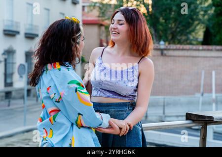 Two happy women couple moment on a city street. They are holding hands, laughing, and enjoying each other's company during a warm evening. Stock Photo