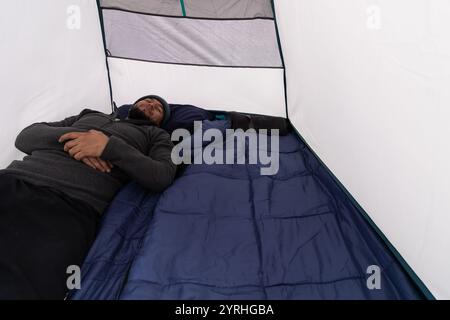 A man peacefully resting inside a tent, surrounded by a cozy sleeping bag during a camping trip Capturing a moment of relaxation and tranquility in na Stock Photo