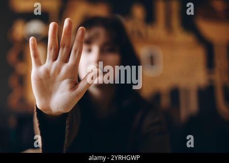 A close-up of a woman's open hand in focus, signaling "stop," with her blurred face in the background. The gesture conveys a clear message of pause or Stock Photo
