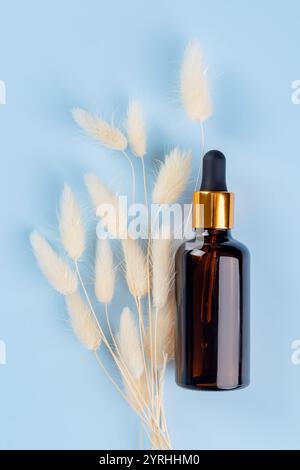 A stylish amber glass dropper bottle is elegantly placed beside soft, natural dried flowers on a soothing blue background, capturing a serene and mini Stock Photo
