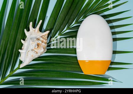 Sun protection cream bottle on green palm leaf with a seashell on a pastel blue background Aesthetic travel and skincare concept for summer vacations Stock Photo