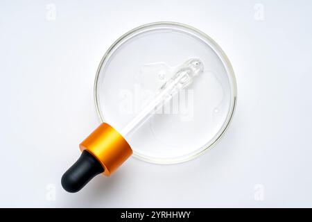 A glass dropper with an orange and black cap resting in a petri dish filled with clear liquid. Ideal for illustrating scientific research or cosmetic Stock Photo