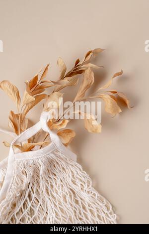 Embrace the simplicity of minimalist design with dry leaves elegantly arranged alongside a white woven bag on a soft beige background Perfect for addi Stock Photo