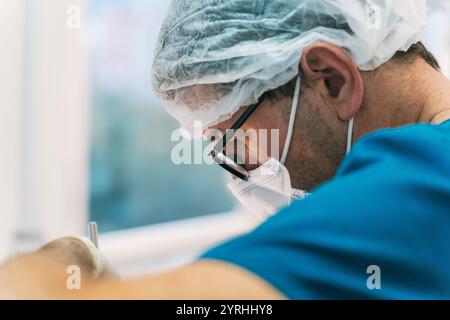 Close-up of a surgeon wearing a mask and cap, focused intensely during a medical procedure. The image portrays precision and concentration in a health Stock Photo