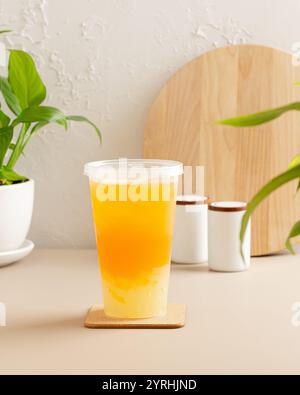 A tall cup of iced tea with a vibrant orange hue sits on a coaster, surrounded by green plants and simple white decor, creating a cozy and modern aest Stock Photo