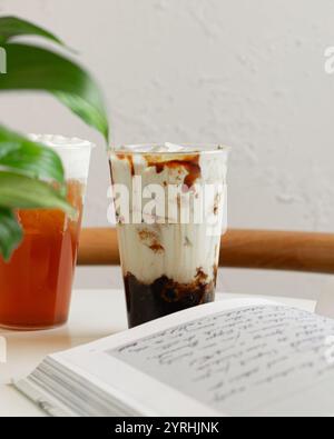 A close-up of two refreshing iced drinks on a table, one with milk tea and the other possibly fruit tea An open notebook and a green plant create a re Stock Photo