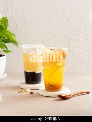 Two refreshing iced teas, one with lemon slices and the other with tapioca pearls, are elegantly served in clear glasses on coasters A green plant com Stock Photo