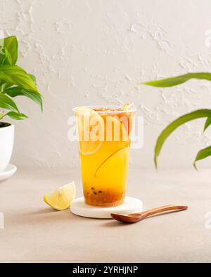 Refreshing iced lemon tea with vibrant citrus slices on a coaster A wooden spoon and fresh green plants create a harmonious, inviting atmosphere again Stock Photo