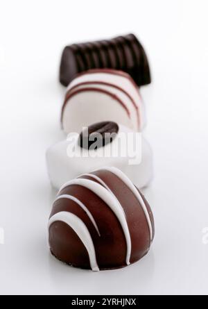 A variety of gourmet chocolate confections are arranged in a row on a white background. The sweets feature intricate designs and are made with both da Stock Photo