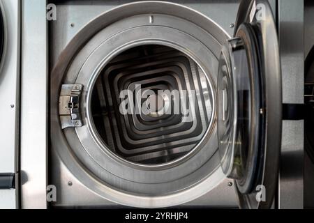 Explore the sleek interior of a modern industrial washing machine, showcasing its intricate silver spiral design and metal finish. Ideal for laundroma Stock Photo
