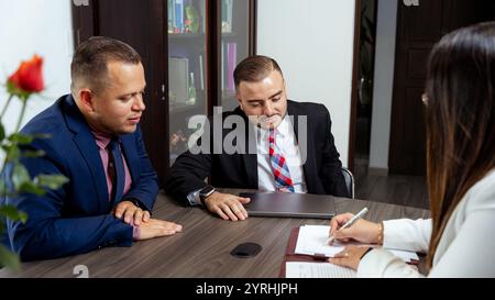 A professional meeting featuring two latino lawyers and a third person reviewing legal documents at a table, emphasizing collaboration, decision-makin Stock Photo