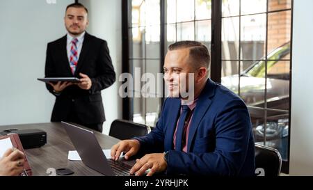 Professionals in suits engaging in a collaborative business meeting One person works on a laptop, while another holds documents, exuding a professiona Stock Photo