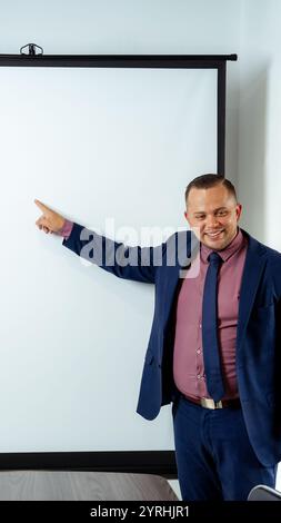 A confident businessman in a formal suit gestures towards a blank presentation screen, suggesting ideas or discussing a project in a professional busi Stock Photo