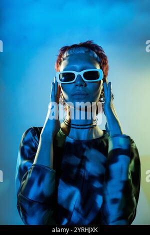 Futuristic woman styled in futuristic blue attire, framed against a gradient blue background Stock Photo