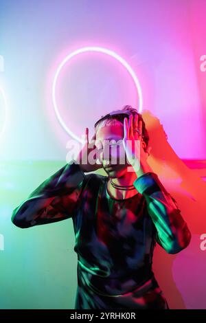 Woman fully engaged in a metaverse space, surrounded by colorful, neon lighting that casts dynamic shadows and highlights on her focused expression an Stock Photo