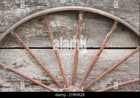 A rusty metal half wagon wheel rests against an aged, textured wooden surface This image captures the essence of rustic decay, perfect for junkyard or Stock Photo