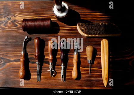 A meticulously arranged set of leather crafting tools on a rustic wooden surface, including awls, thread, and brushes, showcasing the craftsmanship an Stock Photo