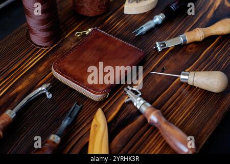 A collection of leather working tools and materials, including a wallet and threads, arranged on a rustic wooden table, showcasing the craft of creati Stock Photo