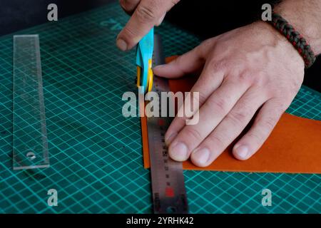 Close-up of a craftsman’s hands carefully cutting leather with a rotary cutter and ruler on a green cutting mat The image captures the precision and c Stock Photo