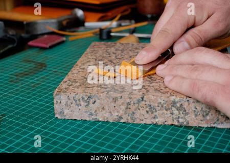 A skilled artisan uses a blade to cut a piece of leather on a granite slab, showcasing craftsmanship in creating leather goods Essential tools are vis Stock Photo