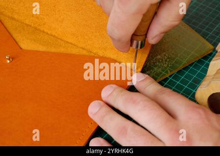 Skilled hands craft an orange leather piece on a green cutting mat, using a precision tool The image captures the intricate process of leather working Stock Photo