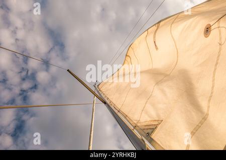 A dynamic view of a sail captured from below, showcasing its texture and the sky's scattered clouds The image conveys freedom and adventure in a nauti Stock Photo
