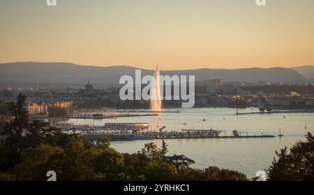 Captivating sunset view over Geneva, Switzerland, showcasing the iconic Jet d'Eau fountain, serene lake, and distant mountains The city skyline is bea Stock Photo