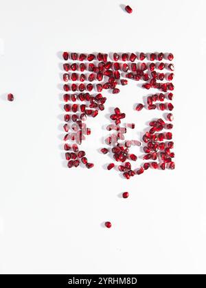 A creative arrangement of scattered pomegranate seeds on a white background. The vibrant red seeds contrast beautifully with the simplicity of the can Stock Photo