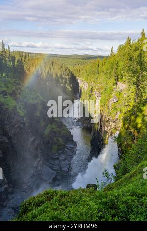 An awe-inspiring view of a waterfall cascading into a vibrant forest valley, illuminated by a rainbow in Swedish Lapland The scene captures nature's r Stock Photo