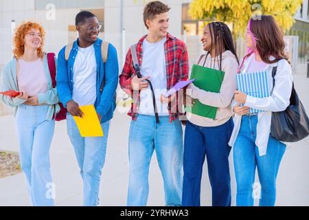 Diverse group of students smiling and walking together outdoors with notebooks Stock Photo
