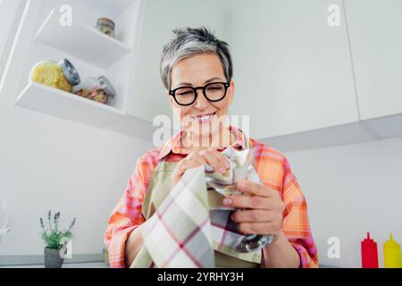 Charming elderly woman enjoying a casual day in her kitchen, preparing with joy. Stock Photo