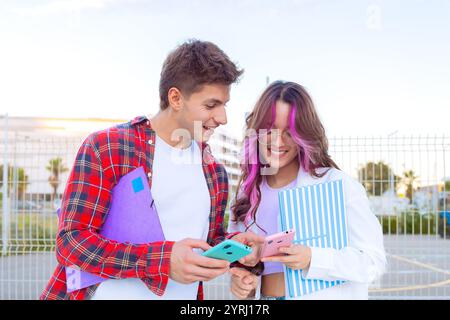 Young students smiling and using smartphones with colorful notebooks outdoors Stock Photo