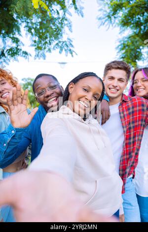 Diverse group of friends waving and smiling outdoors in a cheerful selfie Stock Photo