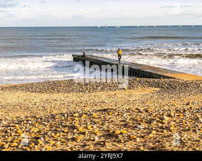 Pebble-strewn beach with a small pier extending into the sea, people standing on the pier enjoying the coastal view on a sunny day blyth south beach Stock Photo