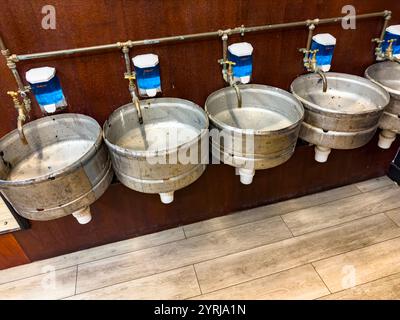 Row of rustic upcycled metal basins in restroom toilets soap dispensers on wooden wall, made from beer barrels alphabetti theatre venue newcastle Stock Photo
