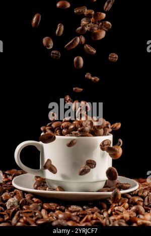 White cup of coffee on black background and coffee beans falling down Stock Photo