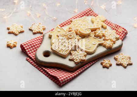 Delicious homemade christmas cookies shaped as snowflakes, gingerbread man, reindeer and houses lying on white cutting board on red checkered tableclo Stock Photo