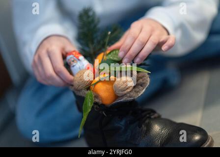 Stuttgart, Germany. 04th Dec, 2024. A girl reaches for a chocolate Santa Claus in a boot filled with mandarins, nuts and twigs. (Staged scene). St. Nicholas Day on 6 December goes back to the legend of two bishops from the 4th and 6th centuries, whose good deeds and stories became the basis of the tradition. Credit: Marijan Murat/dpa/Alamy Live News Stock Photo