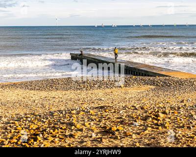 Pebble-strewn beach with a small pier extending into the sea, people standing on the pier enjoying the coastal view blyth south beach  northumberland Stock Photo