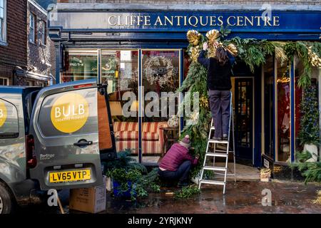 People Putting Up Christmas Decorations Outside An Antique Shop In The High Street, Lewes, East Sussex, UK. Stock Photo