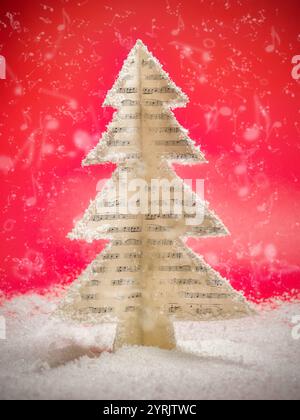 A unique Christmas tree crafted from sheet music stands in a snowy landscape. The red background adds a festive feel, blending music and holiday theme Stock Photo