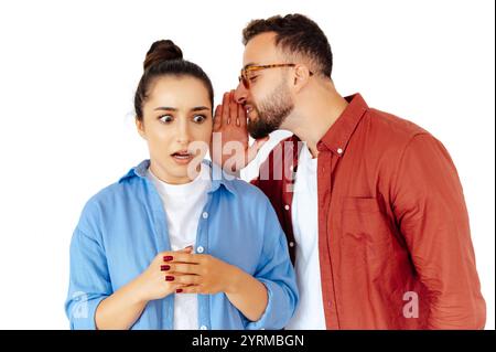 Concerned woman listening to a man whispering in her ear, showing surprise and unease, they dressed in a casual attire, stand on isolated white background Stock Photo