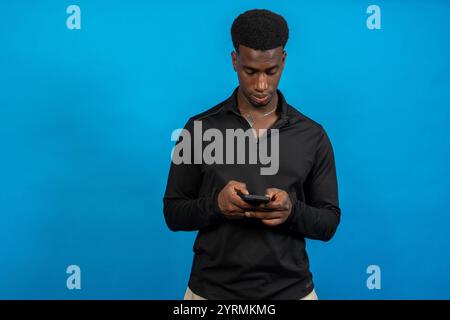 Young man using smartphone on blue background: concentrated young man using mobile phone Stock Photo